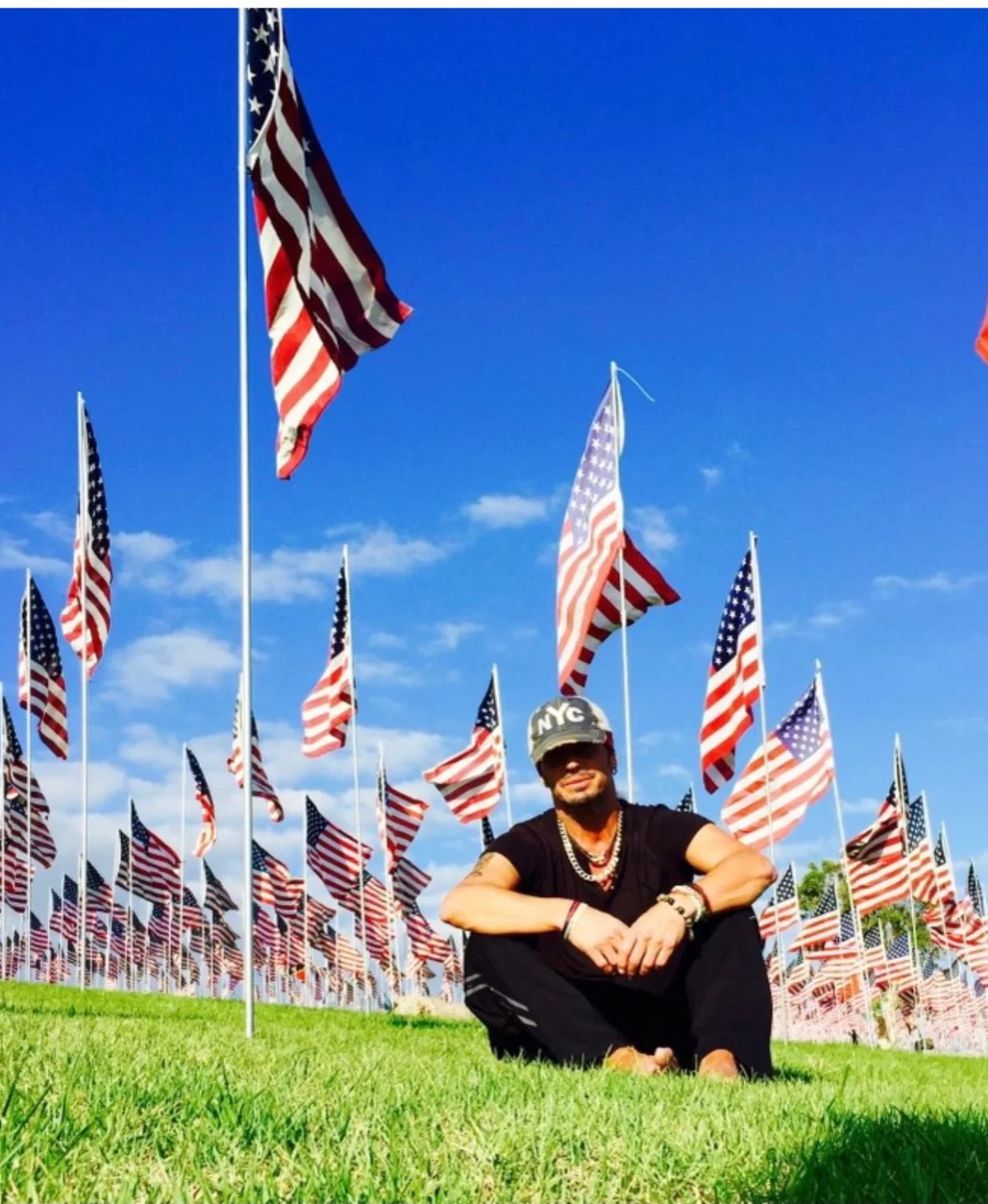 An image of musician and lead singer of rock band, Poison, sitting on a lawn surrounded by USA flags.