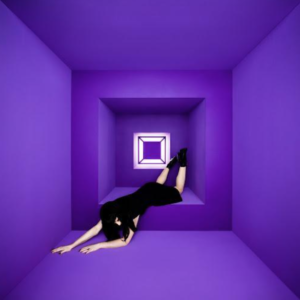 A promotional image of Olivia Jean, pictured face down with legs pushed up against a purple, square wall