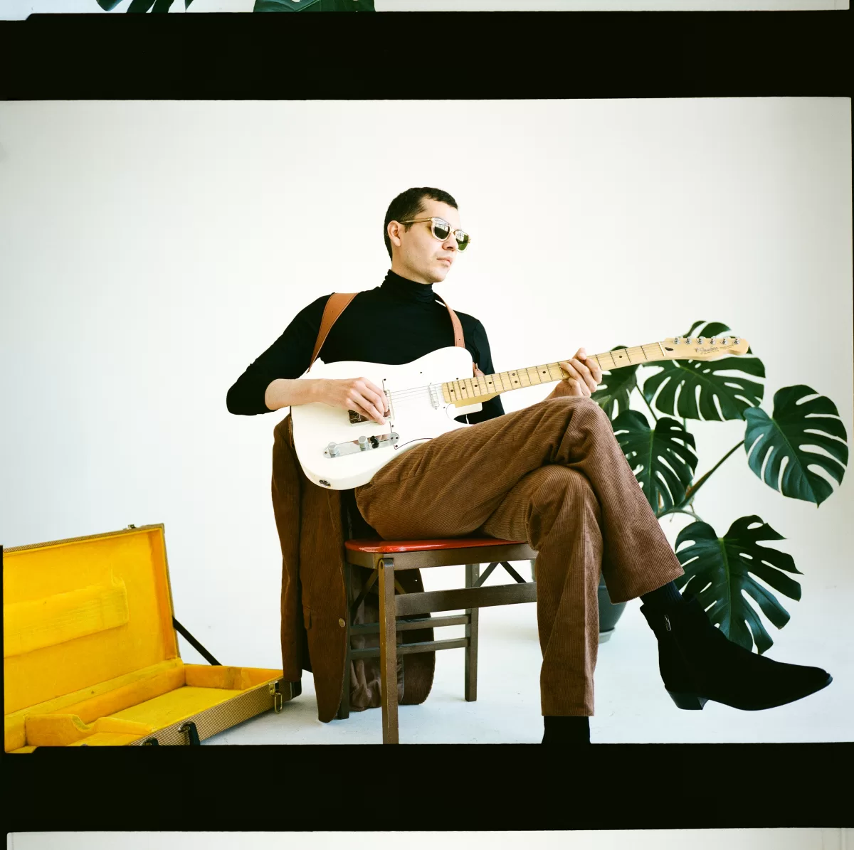 An image of musician and singer, Dani Meza of thecrushedvelvets, sitting with his leg crossed over his leg, strumming a guitar