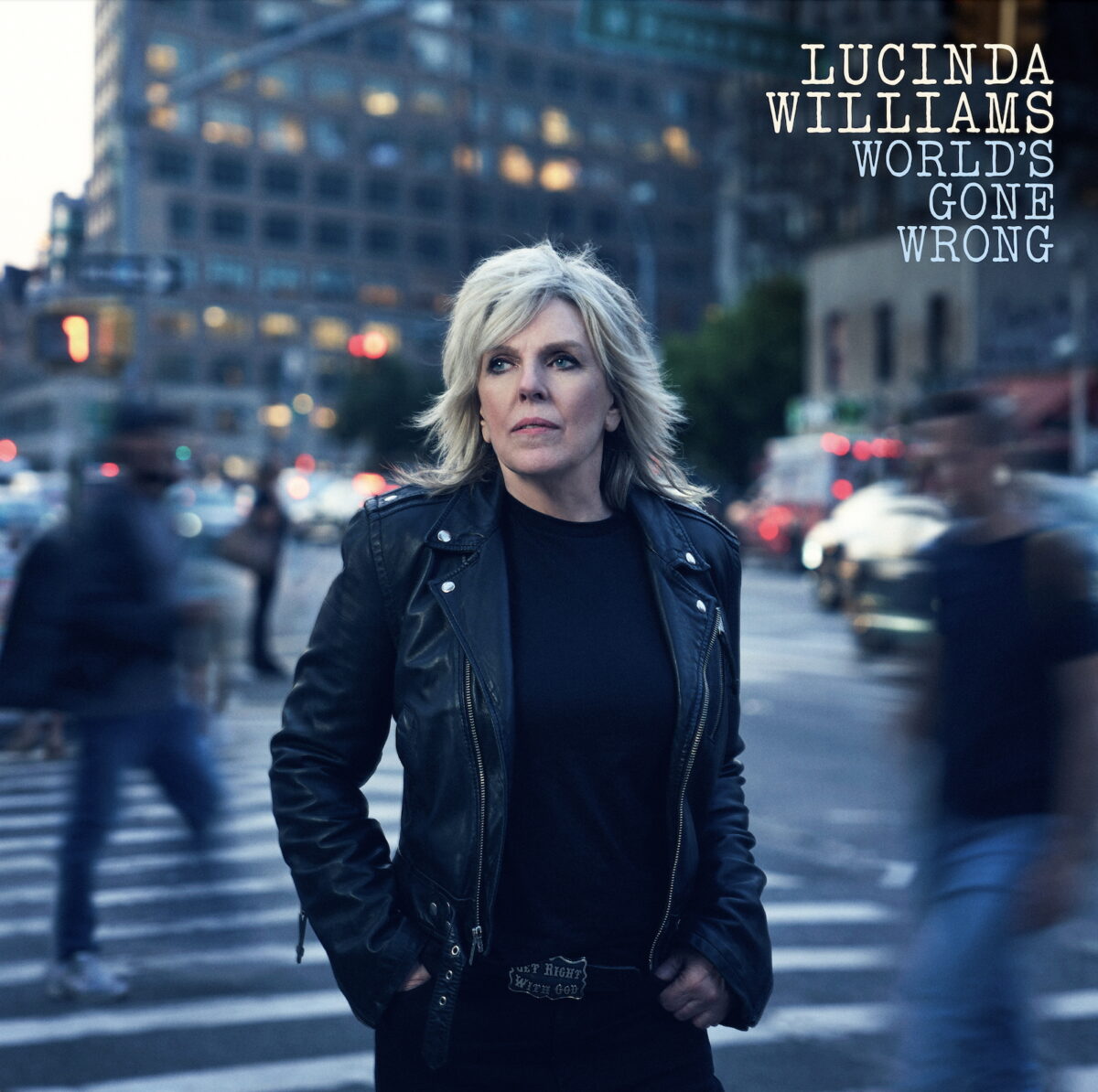 An image of musician and singer, Lucinda Williams, with images of blurred people walking by, and a tall building with lights silhouetted behind her for the cover of her album, World's Gone Wrong