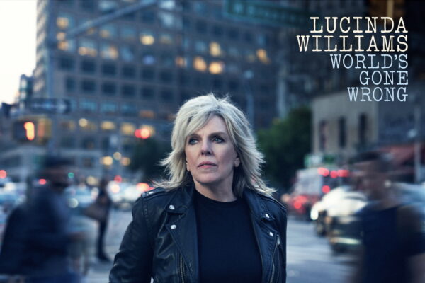 An image of musician and singer, Lucinda Williams, with images of blurred people walking by, and a tall building with lights silhouetted behind her for the cover of her album, World's Gone Wrong